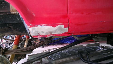 1978 Ford Bronco - Body filler is visible on the lower side panel of a red vehicle, with suspension parts and a wheel in the background.