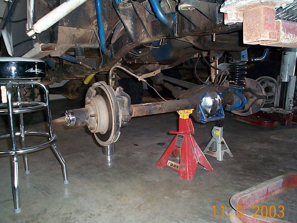 Front axle on jack stands under a lifted vehicle in a garage, hub and rotor exposed