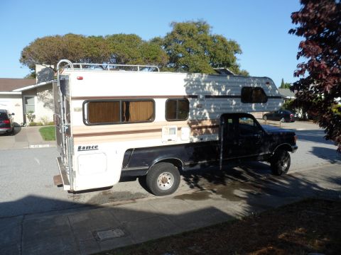1991 Ford Bronco - A black pickup truck is outfitted with a white and tan Lance camper shell, parked on a residential street.
