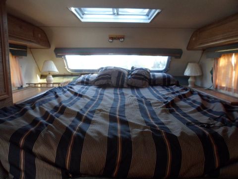 1991 Ford Bronco - The interior of a recreational vehicle features a bed with striped bedding and two bedside lamps.