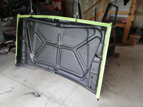 1978 Ford Bronco - The underside of a car hood is taped off and ready for painting in a workshop.