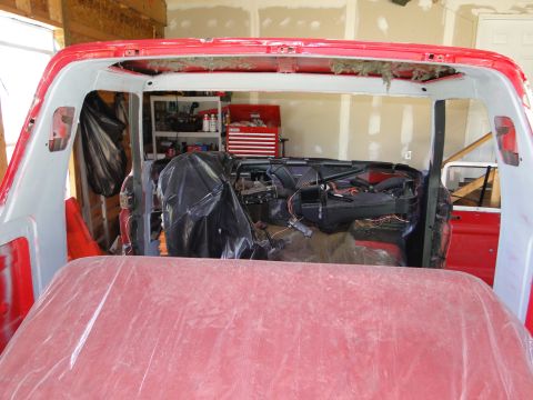 1978 Ford Bronco - Interior of a red vehicle undergoing restoration, showing exposed dashboard and covered seating area.