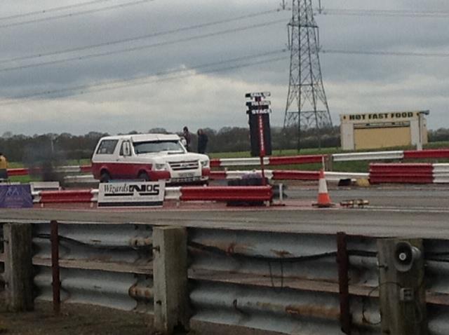 White and red SUV on a drag strip, emitting smoke. Signage visible