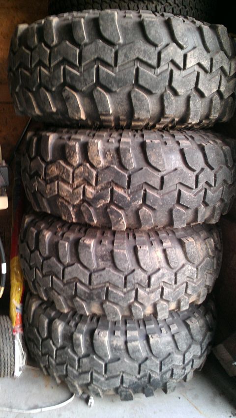 1978 Ford Bronco - A stack of four aggressive tread off-road tires are stored indoors.