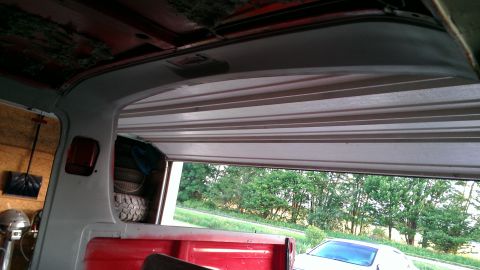 1978 Ford Bronco - The interior of a red truck bed is visible, with a spare tire stacked inside, as the garage door opens to a view of trees.