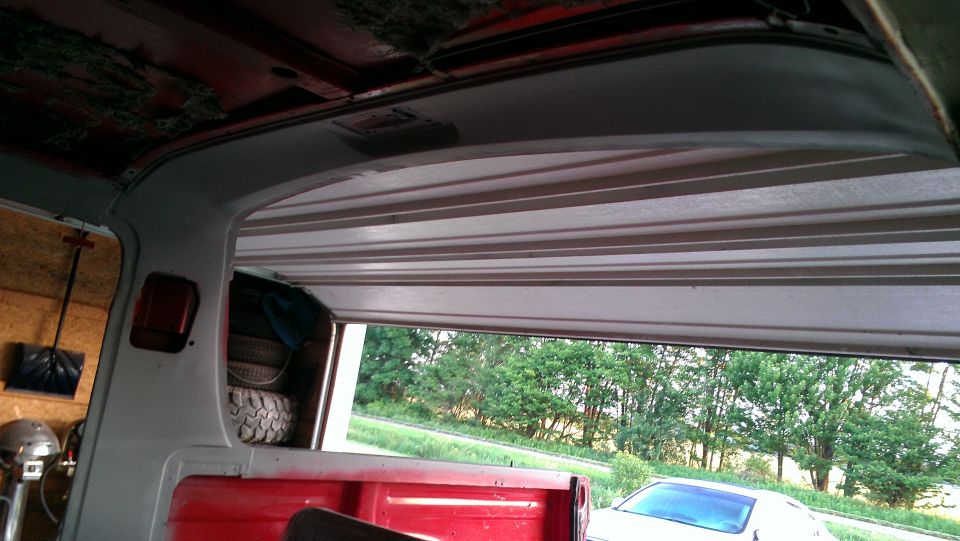Interior view of a red truck bed with a spare tire, looking out an open garage door
