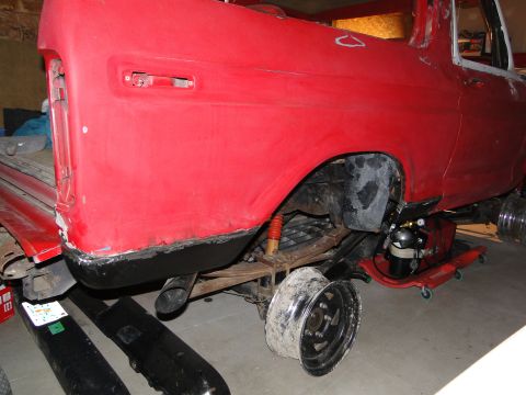 1978 Ford Bronco - The rear of a red 1978 Ford Bronco is shown, with its suspension and a wheel removed, indicating it is in a state of repair.