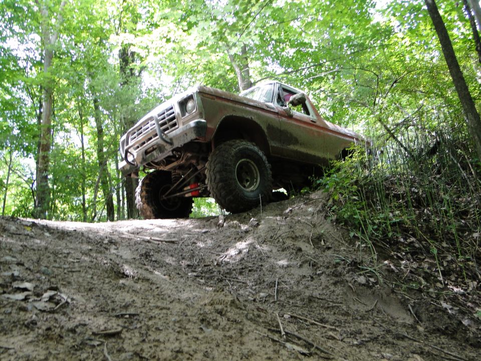 1978 Ford Bronco climbing a muddy hill in a wooded area