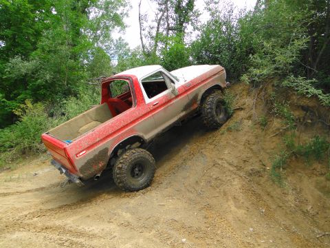 1978 Ford Bronco - This lifted Ford pickup is navigating a steep, muddy incline surrounded by trees.