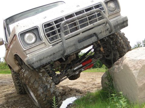 1978 Ford Bronco - A silver Ford truck navigates a challenging off-road course, with its front end angled upwards against a large boulder.
