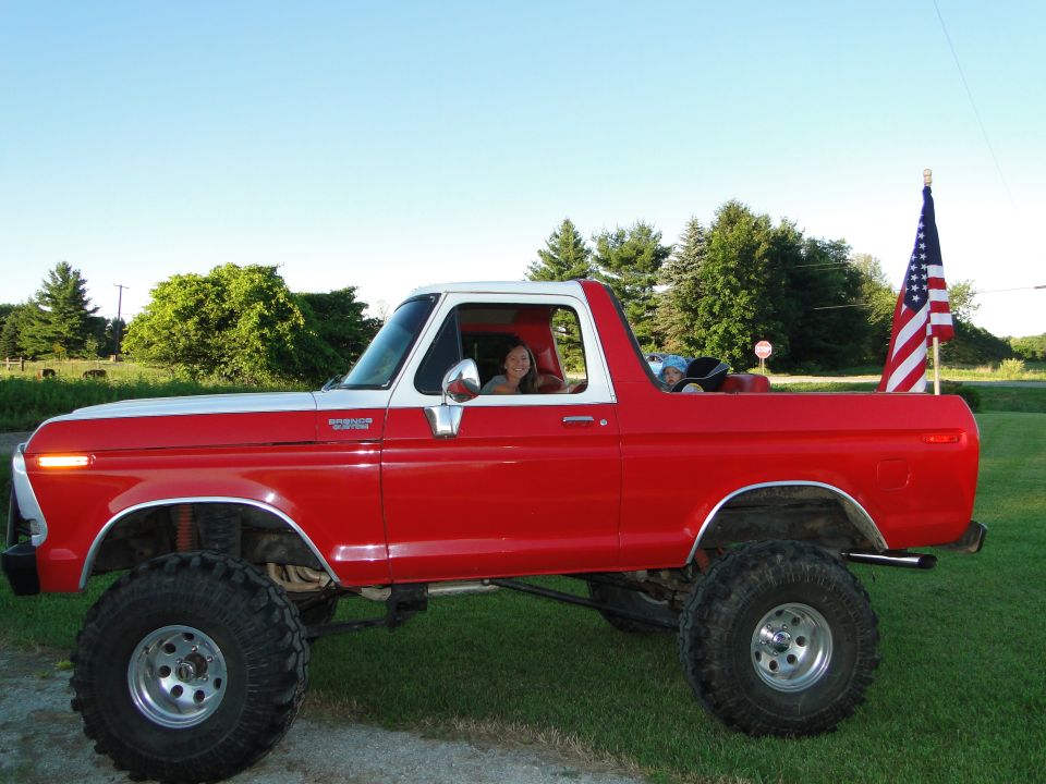 Side view of a lifted red and white 1978 Ford Bronco with an American flag in the background