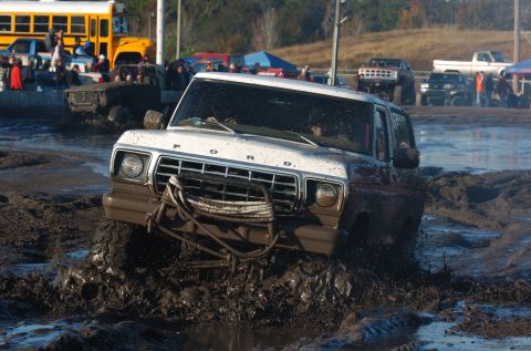 1978 Ford Bronco - A white 1978 Ford Bronco navigates a muddy obstacle course with a yellow school bus in the background.