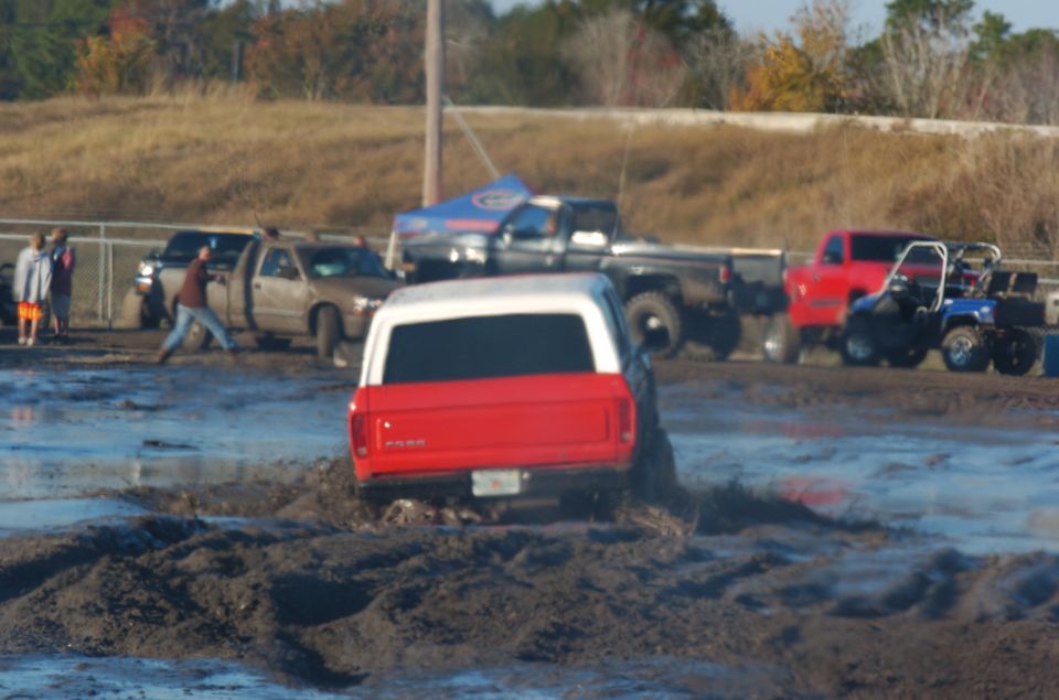 1978 Ford Bronco rear view stuck in mud pit with other vehicles nearby