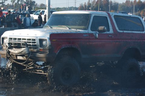 1978 Ford Bronco - This Ford Bronco is navigating a challenging mud pit, with onlookers in the background.