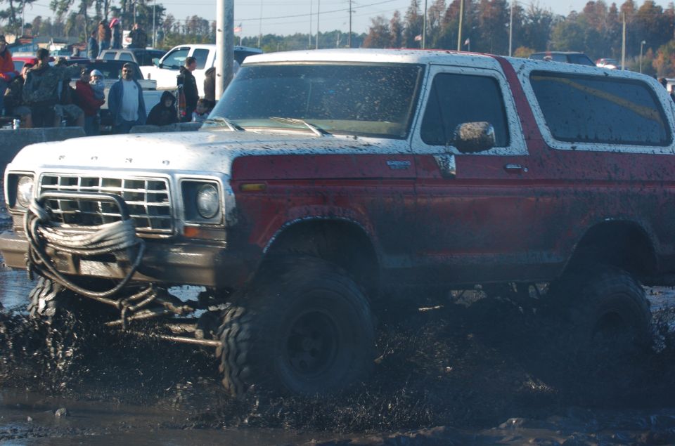 Muddy two-tone red and white Ford Bronco with winch on front bumper going through mud pit