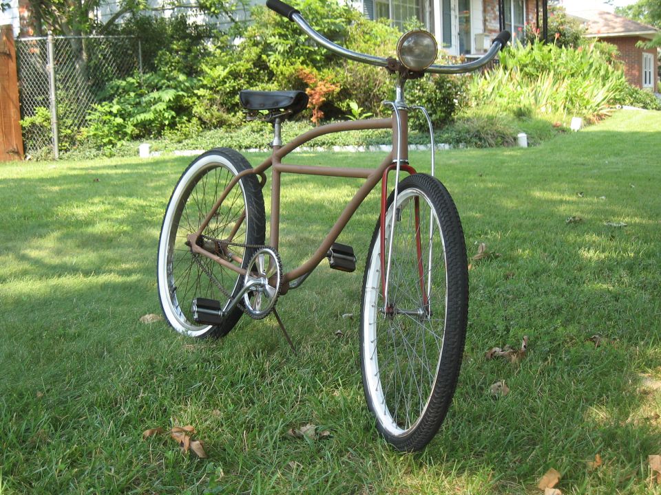 Brown cruiser bicycle with whitewall tires and a headlight, parked on grass