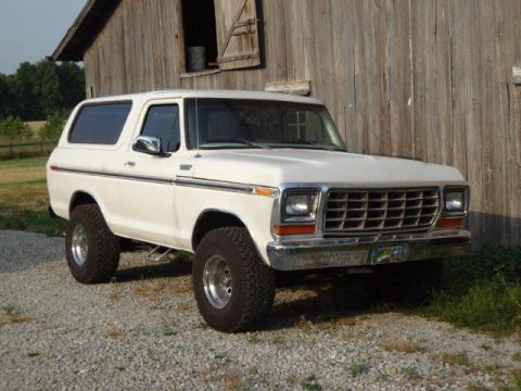 1978 Ford Bronco - A white 1978 Ford Bronco is parked on a gravel surface in front of a rustic wooden barn.