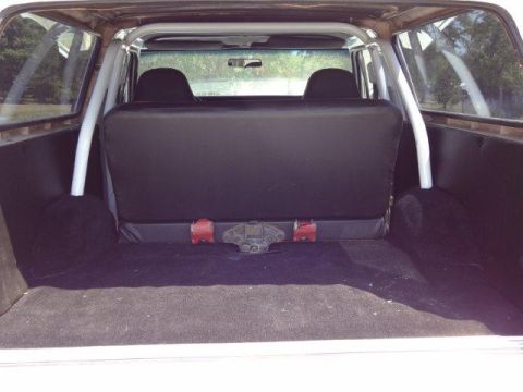 1978 Ford Bronco - The interior of a white SUV is viewed from the rear, revealing black seats and a roll cage.