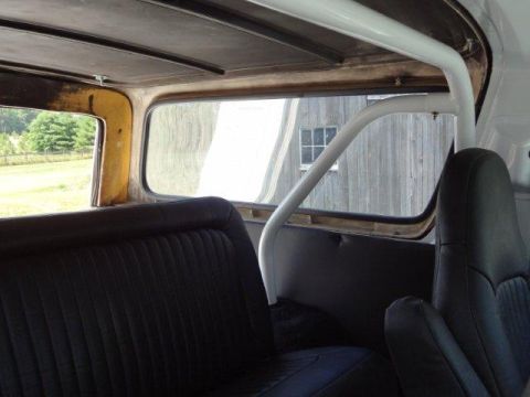 1978 Ford Bronco - The interior of a vintage SUV features black seats and a white roll bar, with a rustic wooden building seen outside.