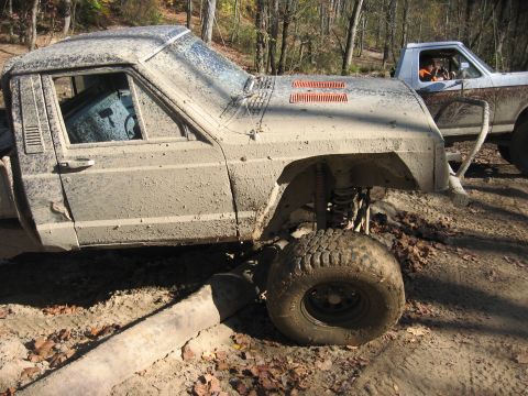 1987 Jeep Comanche - This heavily muddied pickup truck is stuck in the dirt with another vehicle visible behind it.