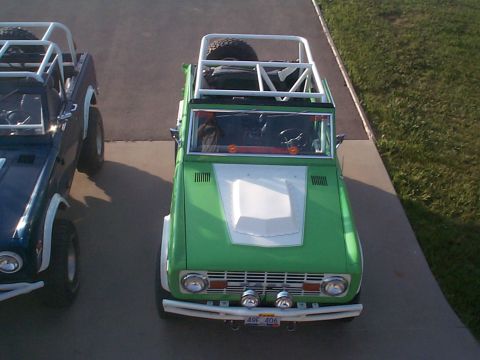 1977 Ford Bronco - Two Ford Broncos, one green and one blue, are parked side-by-side on a paved surface.
