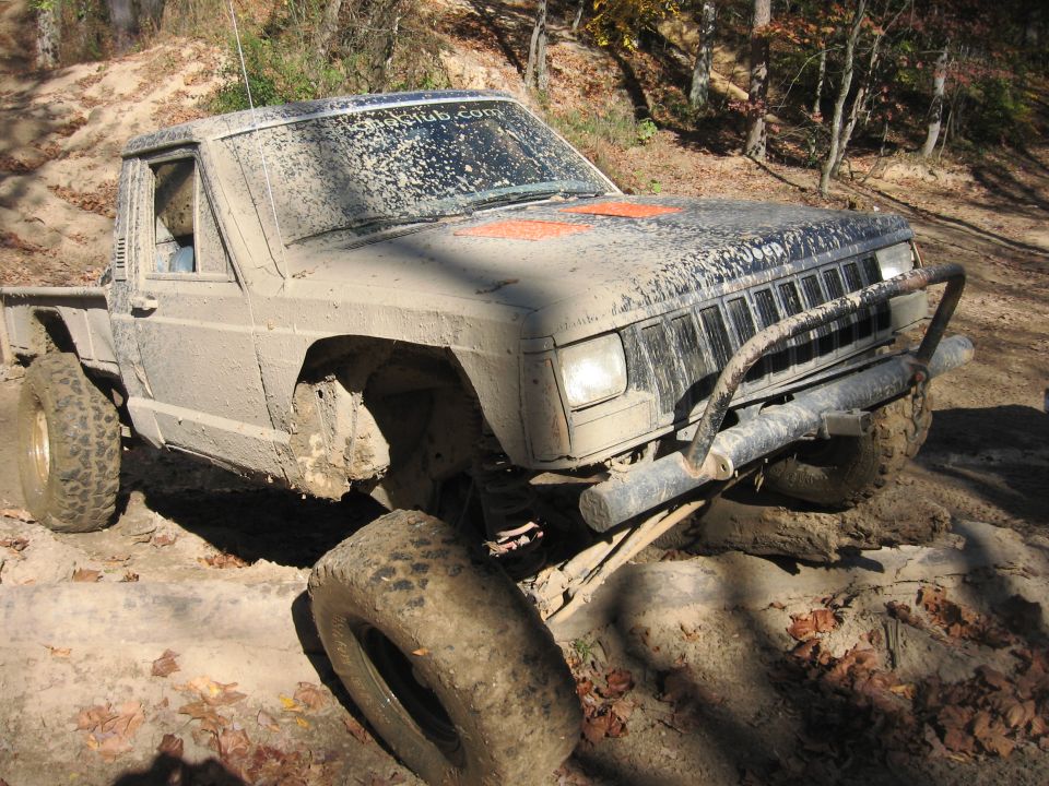 Mud-covered 1987 Jeep Comanche pickup truck navigating rocky terrain