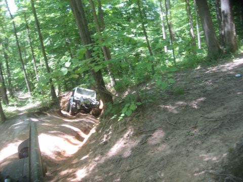 1987 Jeep Comanche - A white Jeep navigates a narrow, rutted dirt path surrounded by dense forest foliage.