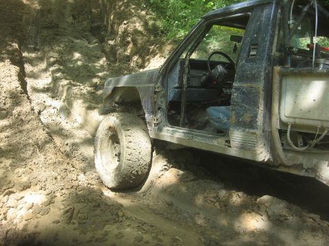 1987 Jeep Comanche - A heavily modified 1987 Jeep Comanche navigates a challenging off-road trail, its tires deep in mud.