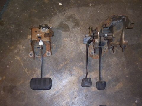 1991 Ford LTD Crown Victoria - Two pedal assemblies laid side by side on a concrete floor for comparison: at left a single wide automatic-transmission brake pedal on its…