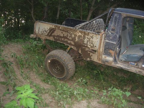 1987 Jeep Comanche - This heavily soiled pickup truck is partially obscured by overgrown vegetation and appears to be stuck on a muddy embankment.