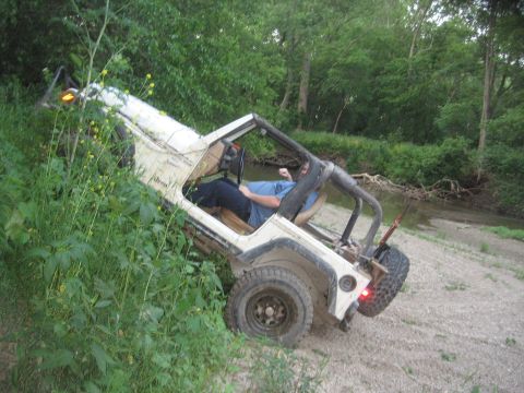 1987 Jeep Comanche - A white Jeep pickup truck is partially off-road, leaning precariously on a bank beside a shallow stream.