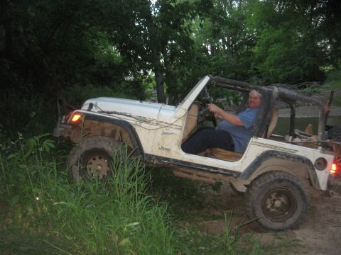 1987 Jeep Comanche - A driver navigates a white Jeep Wrangler through a muddy, wooded trail.