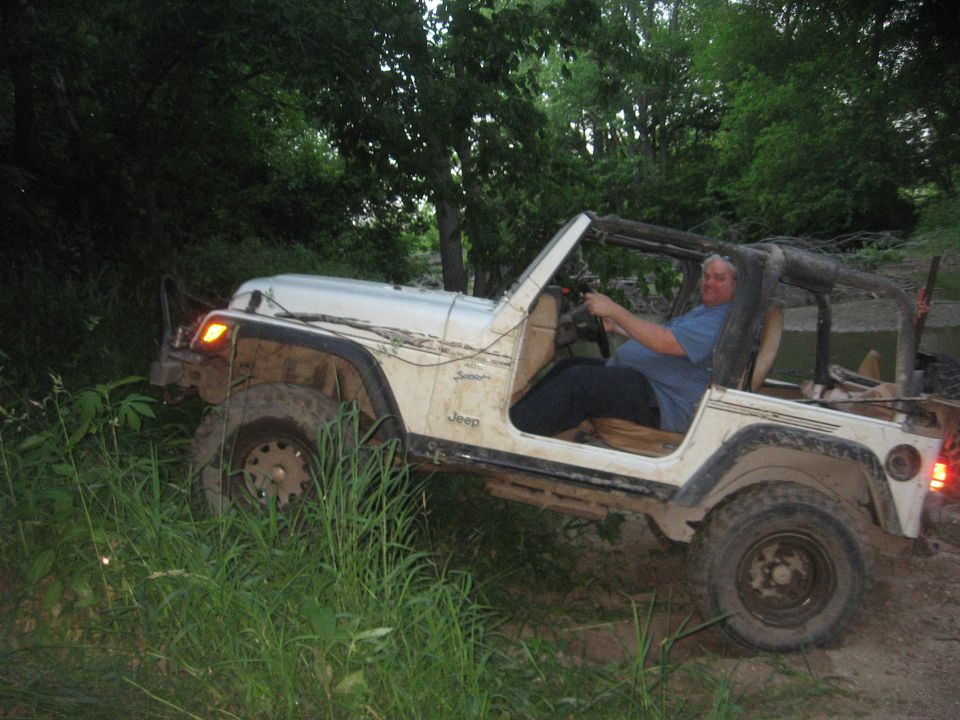 White Jeep Wrangler with a driver off-roading in a wooded area
