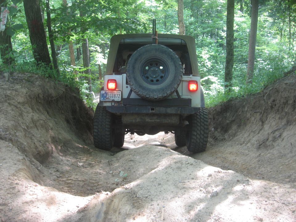 Jeep Wrangler TJ driving on a dirt trail through woods, rear view
