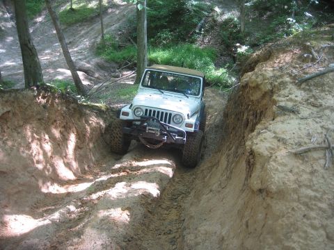 1987 Jeep Comanche - A white Jeep Wrangler tackles a challenging off-road trail, with visible tire tracks in the dirt.