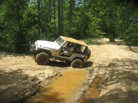 1987 Jeep Comanche - A Jeep Wrangler TJ navigates a muddy obstacle on a wooded trail.