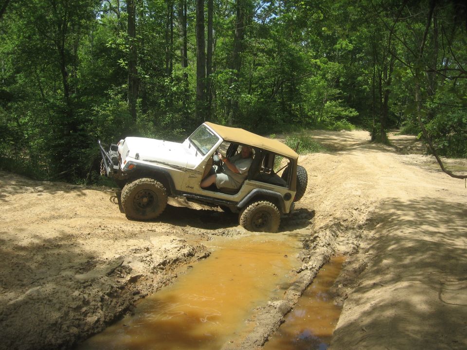 White Jeep Wrangler TJ driving through a muddy trail in the woods