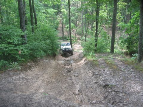 1987 Jeep Comanche - A white Jeep Wrangler navigates a challenging muddy path through a dense forest.