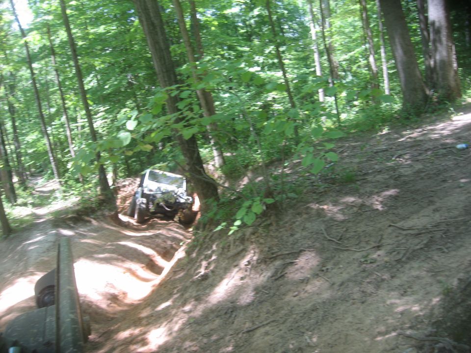 White Jeep Comanche driving on a dirt trail in a forest, viewed from a low angle