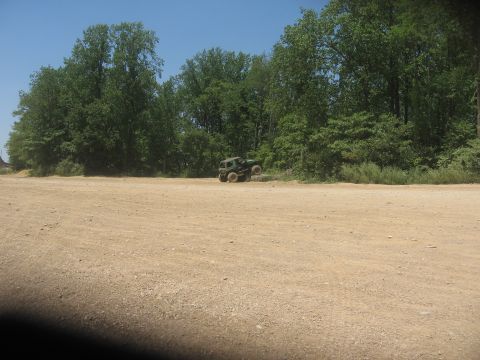 1987 Jeep Comanche - A green off-road vehicle is parked on a dirt lot with trees in the background.