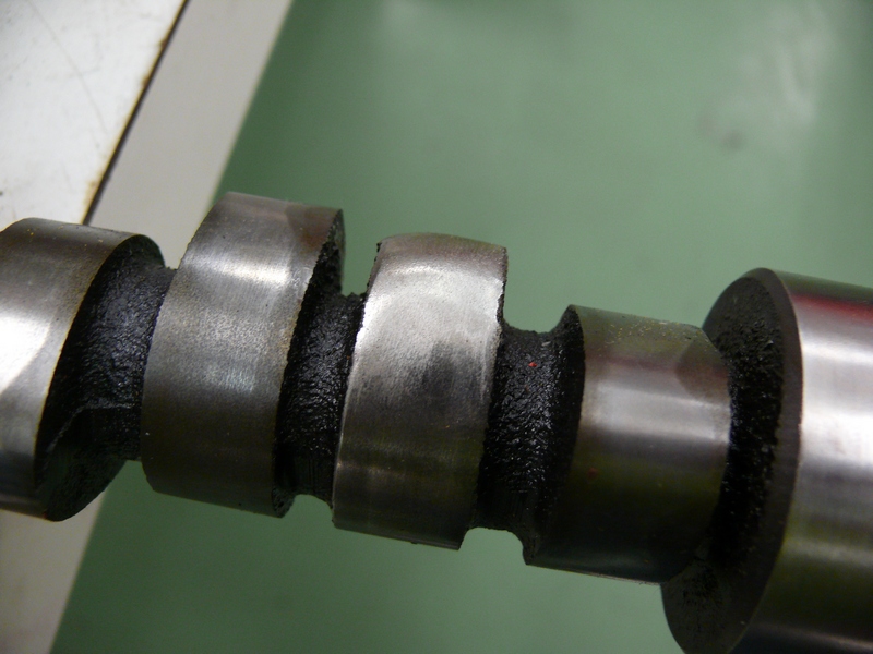 Camshaft with worn lobes and black coating, close-up view