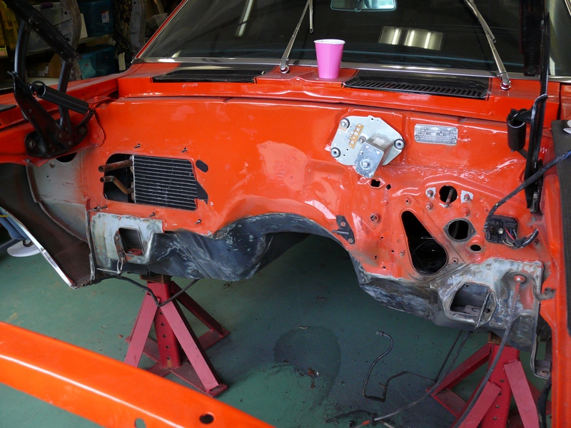 Car's engine bay, orange paint, missing engine, on jack stands. Pink cup on dash