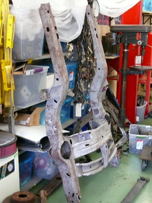 Rusty car frame sections hanging, with wiring and storage shelves in background