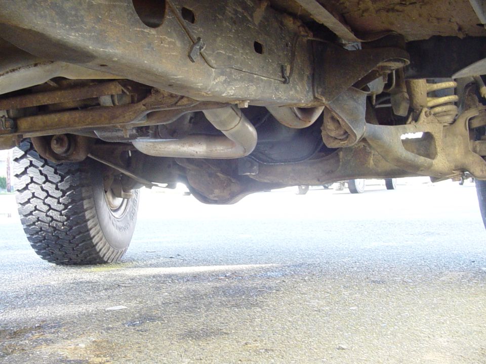 Undercarriage of a lifted 4x4 showing rusty frame, dual exhaust and driveshaft