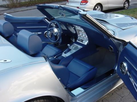 1976 Chevrolet Corvette - The interior of a silver convertible with a blue leather interior is shown, with the driver's side door ajar.