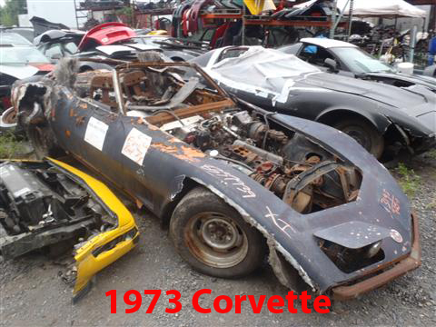 1976 Chevrolet Corvette - This heavily damaged Corvette is in a junkyard, with visible engine parts and rust.
