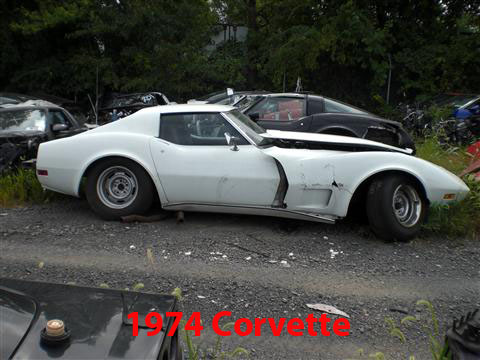 1976 Chevrolet Corvette - A damaged white 1974 Chevrolet Corvette sits in a junkyard next to other vehicles.