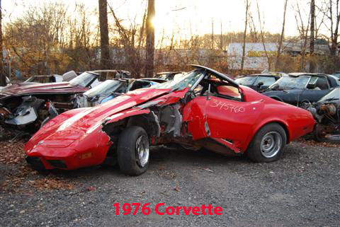 1976 Chevrolet Corvette - This heavily damaged red 1976 Chevrolet Corvette sits in a junkyard, surrounded by other wrecked vehicles.