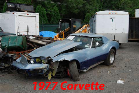 1976 Chevrolet Corvette - This heavily damaged Chevrolet Corvette sits in a junkyard with its hood open and front end destroyed.