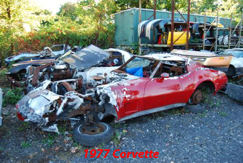 1976 Chevrolet Corvette - A heavily damaged red Chevrolet Corvette sits in a junkyard, surrounded by other wrecked vehicles.